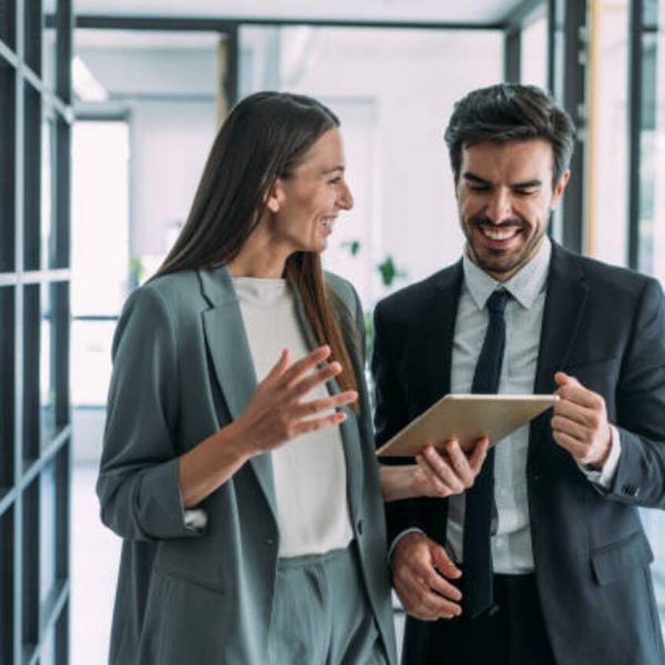 Shot of two coworkers having a discussion in modern office. Businessman and businesswoman in meeting using digital tablet and discussing business strategy. Confident business people working together in the office. Corporate business persons discussing new project and sharing ideas in the workplace.